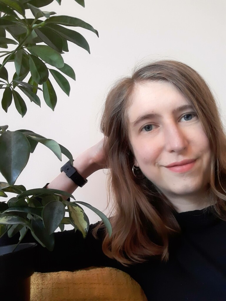 Frances Pope, a white woman with long hair sitting next to a green plant.