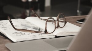 Glasses placed on a notebook next to a laptop